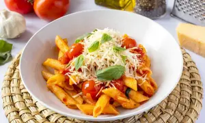 Un plato de macarrones a la napolitana con salsa de tomate, tomates cherry, albahaca fresca y queso rallado.