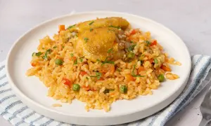 Un plato de arroz con pollo, guisantes, zanahoria y pimiento rojo, adornado con perejil picado.