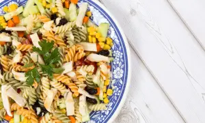 Ensalada de pasta con pollo, pepino, maíz y pasas, decorada con perejil fresco. Un plato colorido y nutritivo.
