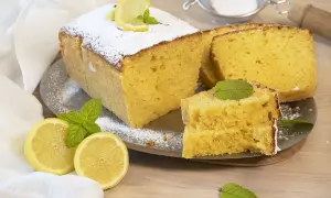 Un delicioso bizcocho de limón, espolvoreado con azúcar glas y decorado con rodajas de limón y hojas de menta.