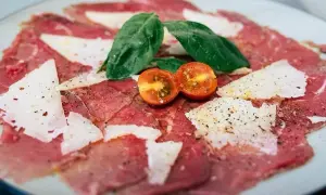 Delicado carpaccio de ternera con lascas de parmesano, hojas de albahaca y tomates cherry.