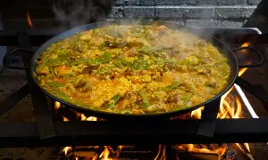 Arroz con carne humeante en paellera sobre fuego vivo. Judías verdes y trozos de carne se mezclan con el arroz dorado.
