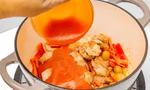 Se vierte salsa de tomate sobre trozos de pollo y pimientos en una olla.