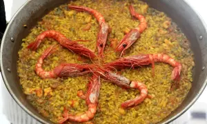 Arroz con carabineros, un plato de paella con gambas rojas grandes dispuestas en círculo sobre el arroz amarillo.