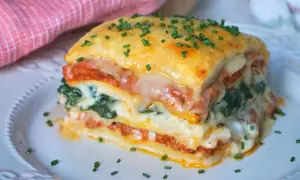 Porción de lasaña de espinacas, con capas de pasta, salsa de tomate, queso derretido y espinacas, espolvoreada con cebollín.