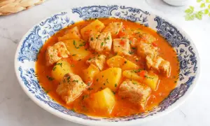 Un delicioso marmitako de atún con patatas y pimientos rojos, servido en un plato con borde azul y blanco.