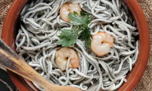 Gulas al ajillo servidas en cazuela de barro, con gambas y perejil. Una cuchara de madera lista para servir.