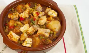 Un delicioso marmitako de salmón, con trozos de pescado, patatas, guisantes y pimientos rojos en una cazuela de barro.