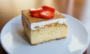 Un trozo de tarta 3 leches, esponjoso y cubierto con crema batida, canela y fresas frescas.