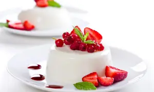 Deliciosa panna cotta receta, decorada con fresas, grosellas rojas y menta.