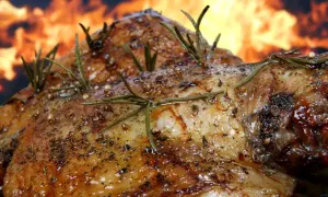 Pierna de cordero al horno, dorada y jugosa, con romero y especias, sobre un fondo de llamas. ¡Un festín irresistible!