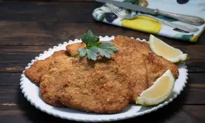Milanesa de ternera dorada y crujiente, servida en plato blanco con gajos de limón y perejil.