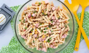 Ensalada de pasta con jamón, guisantes y maíz, lista para servir con su salsa para ensalada de pasta.