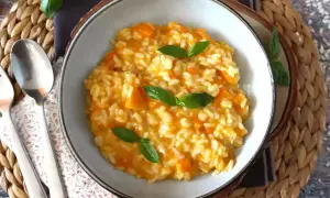 Cremoso risotto de calabaza, adornado con hojas de albahaca fresca, servido en un cuenco rústico.