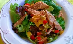 Ensalada de ventresca con pimientos de colores y semillas de sésamo, servida sobre hojas verdes frescas.