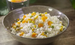 Un plato de arroz blanco con guisantes, maíz y zanahoria en cubitos. Una receta de arroz con verduras sencillo y colorido.