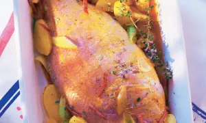 Pescado rosado al horno con patatas y hierbas aromáticas en una bandeja blanca.