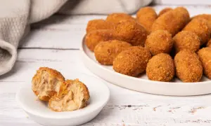 Croquetas de puchero doradas y crujientes, una de ellas partida mostrando su interior cremoso.