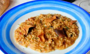 Un cremoso risotto de boletus, adornado con hierbas frescas, servido en un plato azul y blanco.