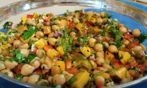 Ensalada de legumbres vibrante con garbanzos, pimientos de colores, cebolla morada y cilantro fresco, todo mezclado en un bol de vidrio.