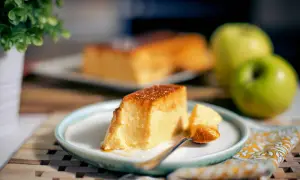 Un delicioso flan de manzana, con una porción servida en plato, junto a manzanas verdes y una planta.