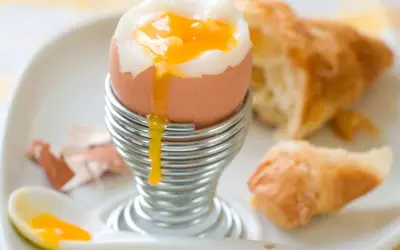 Un huevo pasado por agua con su yema dorada cayendo, listo para ser disfrutado con un croissant.