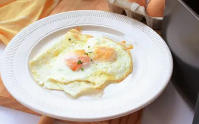 Dos huevos fritos perfectos, cocinados en freidora de aire, servidos en un plato blanco. Un toque de cebollino fresco adorna las yemas.