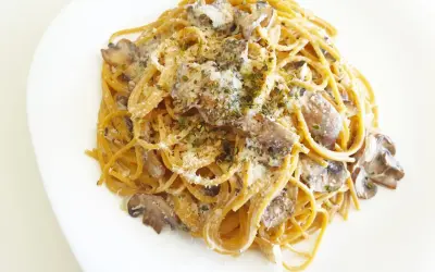 Espaguetis con nata y champiñones, cubiertos con queso rallado y hierbas aromáticas. Un plato cremoso y delicioso.