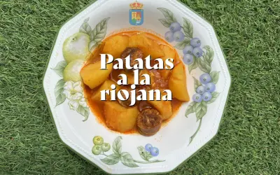 Un plato de patatas a la riojana, con trozos de chorizo y patata en una salsa rojiza, servido en una vajilla decorada con frutas y bayas.