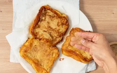 Torrijas de horchata doradas y crujientes, listas para disfrutar. Una mano espolvorea azúcar y canela sobre una de ellas.