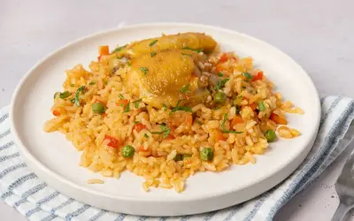 Un plato de arroz con pollo, guisantes, zanahoria y pimiento rojo, adornado con perejil picado.