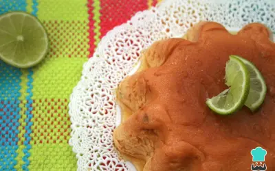 Delicioso flan de limón con rodajas de lima, servido sobre un mantel colorido y un encaje blanco.