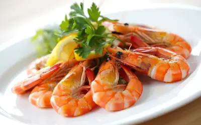 Deliciosas gambas al ajillo servidas en un plato blanco, adornadas con perejil fresco y rodajas de limón.