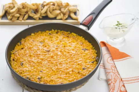 Arroz con sepia en paellera, acompañado de patatas fritas y una salsa cremosa.