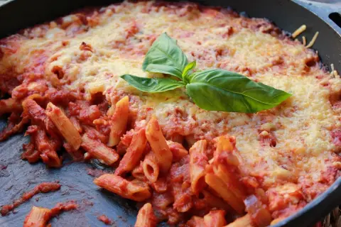Macarrones al horno con salsa de tomate y queso gratinado, decorados con hojas de albahaca fresca. ¡Un plato casero irresistible!