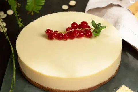 Deliciosa tarta de chocolate blanco, coronada con grosellas rojas y menta fresca. Un postre elegante y cremoso.