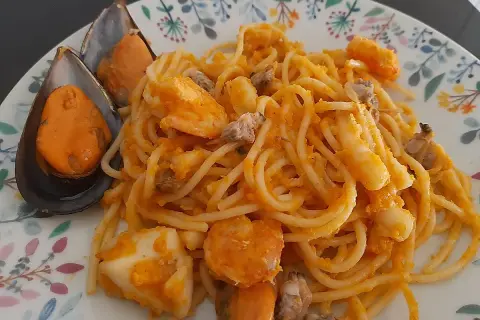Espaguetis a la marinera con mejillones, gambas y calamares, servidos en un plato con un delicado estampado floral.