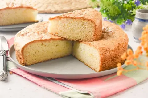 Bizcocho sin huevo esponjoso y dorado, cortado en porciones sobre un plato gris. Ideal para desayunos o meriendas.