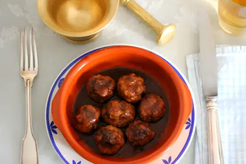 Un cuenco de barro con deliciosas albóndigas en salsa, listo para ser disfrutado con tenedor y cuchillo.