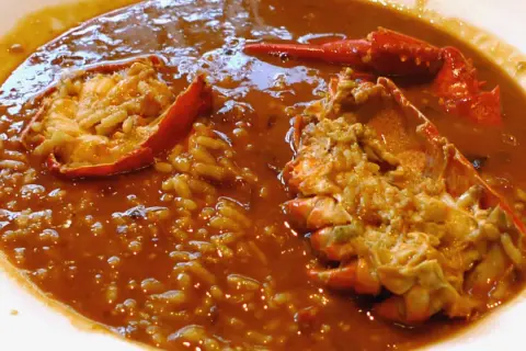 Delicioso arroz caldoso de marisco con trozos de langosta en un plato blanco.