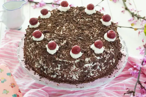 Deliciosa tarta Selva Negra, cubierta de virutas de chocolate y coronada con cerezas y nata. Perfecta para cualquier celebración.