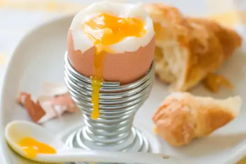 Un huevo pasado por agua con su yema dorada cayendo, listo para ser disfrutado con un croissant.