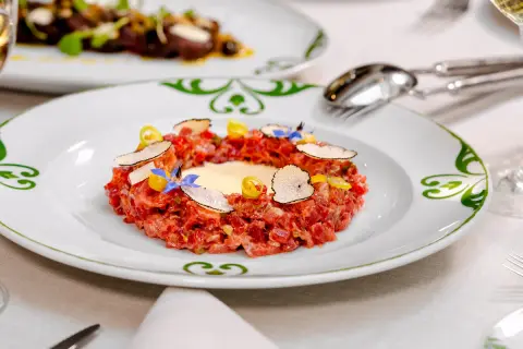 Delicioso tartar de atún fresco, adornado con láminas de trufa negra, flores comestibles y un toque de limón.