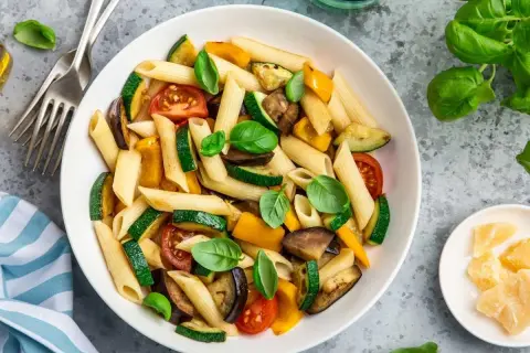 Macarrones con verduras asadas: calabacín, berenjena, pimientos y tomates, decorados con albahaca fresca. ¡Una forma deliciosa de aprender como hacer macarrones!