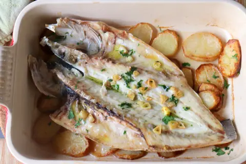 Lubina a la espalda horneada con patatas, ajo y perejil en una bandeja.