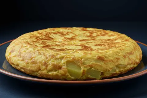 Tortilla de berenjena dorada y esponjosa, con trozos de patata visibles, servida en un plato azul.
