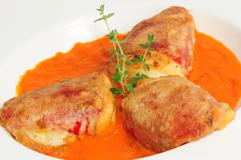Pimientos rellenos de bacalao, dorados y crujientes, servidos en una cremosa salsa de pimientos rojos, adornados con tomillo fresco.