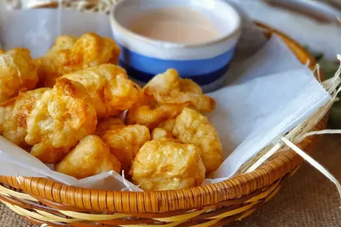 Cesta de mimbre con fritos de pixin dorados y crujientes, acompañados de una salsa rosada. ¡Un bocado delicioso!