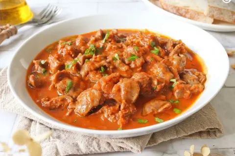 Mollejas de pollo en salsa roja, un plato casero y reconfortante, servido en un cuenco blanco con perejil picado.