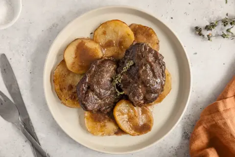 Dos jugosas galtas al horno, tiernas y cubiertas de salsa, servidas sobre rodajas de patata dorada. Un plato reconfortante.